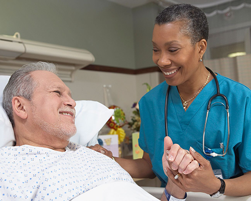 A nurse holding a patient's hand in a hospital room.