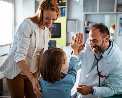 A doctor high-fives a child during a consultation while the child's mother smiles.