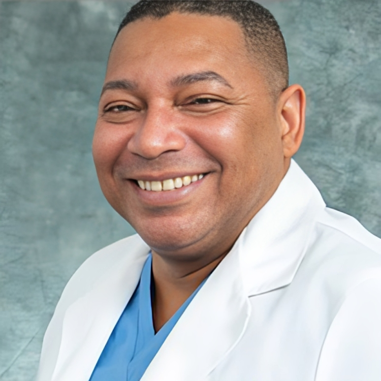 Person in white lab coat with a blue scrub top, against a mottled grey background.